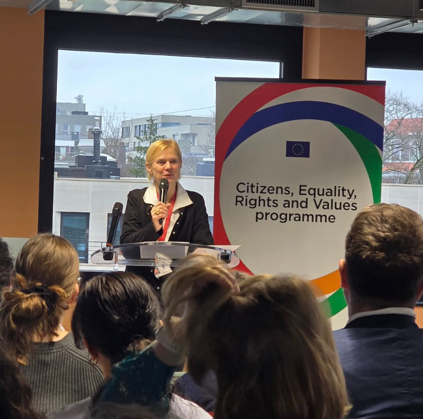 Una relatrice interviene al microfono davanti al pubblico, accanto al roll-up del programma europeo 