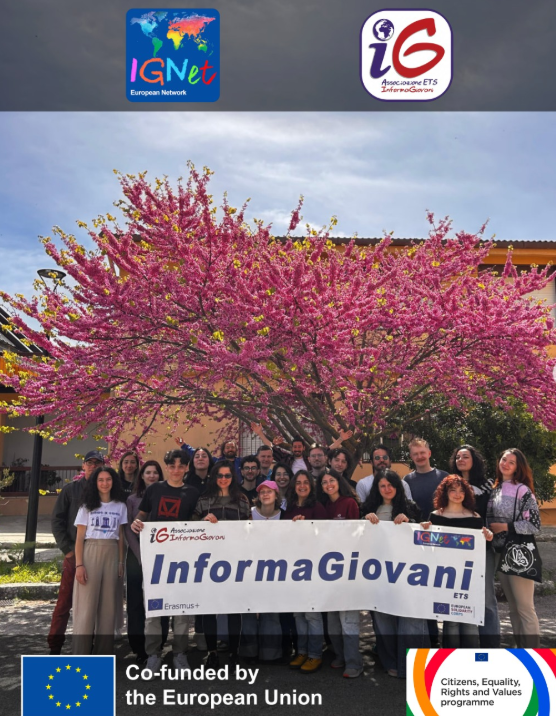 I partecipanti al Leader Training 2026 posano in gruppo sotto un albero di Giuda in piena fioritura rosa, reggendo lo striscione di InformaGiovani; in alto i loghi della rete IGNet e dell'associazione, in basso quelli del cofinanziamento dell'Unione Europea e del programma CERV.