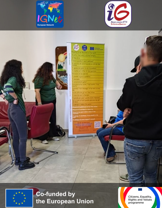 Le operatrici di InformaGiovani presentano ai giovani dell'USSM il roll-up del Violentometro, la scala colorata che aiuta a riconoscere i segnali d'allarme nelle relazioni, dai comportamenti più sottili a quelli apertamente violenti; in alto i loghi della rete IGNet e dell'associazione, in basso quelli del cofinanziamento dell'Unione Europea e del programma CERV.