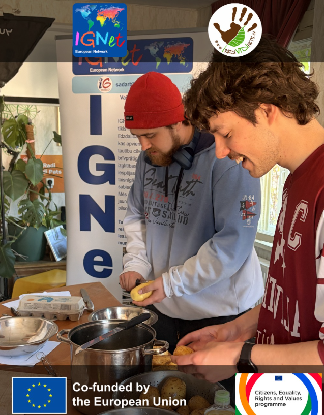 Due persone sbucciano le patate durante il laboratorio interculturale di cucina spagnola organizzato da Radi Vidi Pats, accanto al roll-up della rete IGNet con il testo in lettone; in alto i loghi della rete IGNet e di Radi Vidi Pats, in basso quelli del cofinanziamento dell'Unione Europea e del programma CERV.