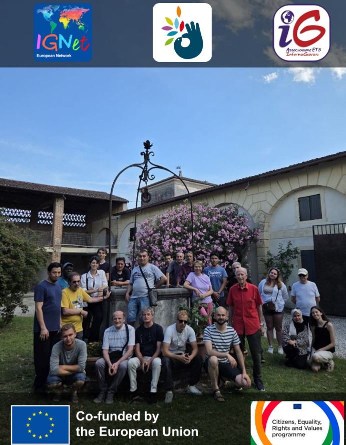 olontari internazionali, volontari locali e persone accolte dalla comunità Emmaus posano insieme attorno al pozzo in ferro battuto nel cortile della comunità di Villafranca di Verona, tra gli edifici rurali e un grande oleandro in fiore