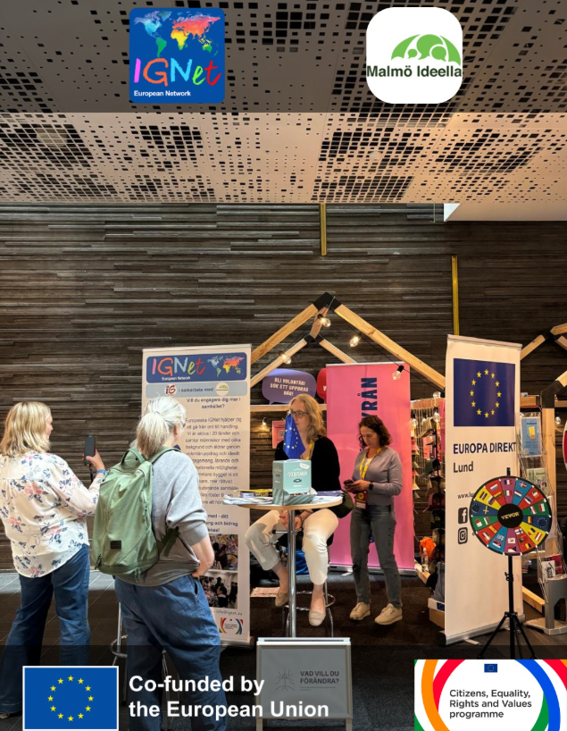 Lo stand informativo della rete IGNet a un evento pubblico in Svezia, con il roll-up della rete in svedese, il banner di Europa Direkt Lund con la ruota delle bandiere europee e alcune visitatrici in conversazione con le operatrici; in alto i loghi della rete IGNet e di Malmö Ideella, in basso quelli del cofinanziamento dell'Unione Europea e del programma CERV.