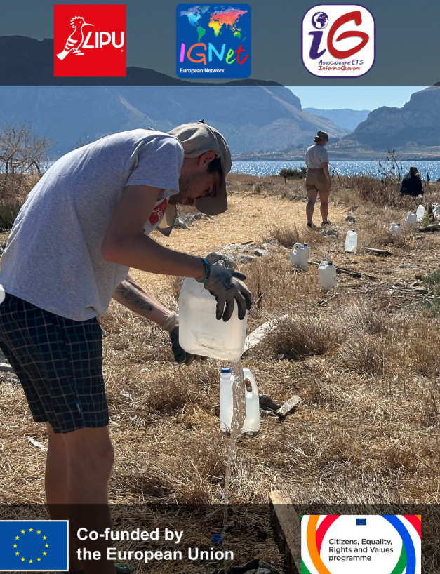 Un volontario con i guanti versa acqua da una tanica in un contenitore accanto alle giovani piante, lungo un sentiero di terra battuta con il mare e le montagne della costa sullo sfondo.