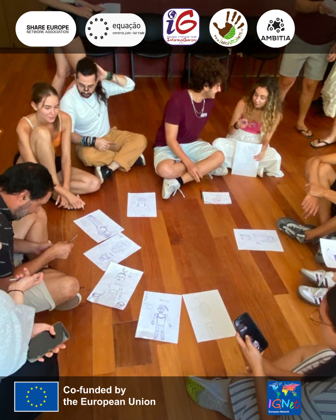 gruppo di persone sedute in cerchio, ogni persona ha il proprio foglio posizionato davanti a sè sul pavimento