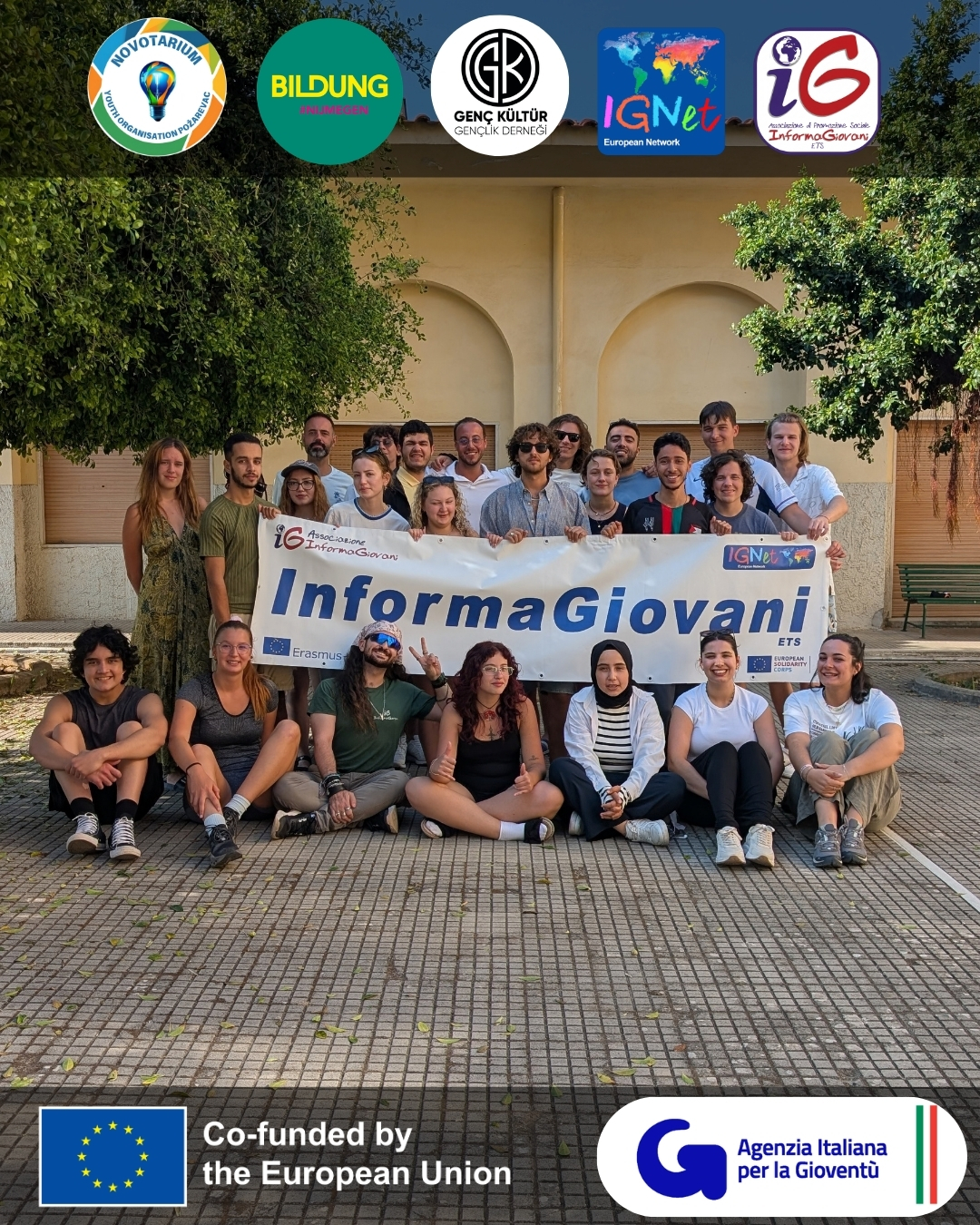 Foto di gruppo dei partecipanti, alcuni seduti a terra e altri in piedi, con un banner di Informagiovani esposto in primo piano.