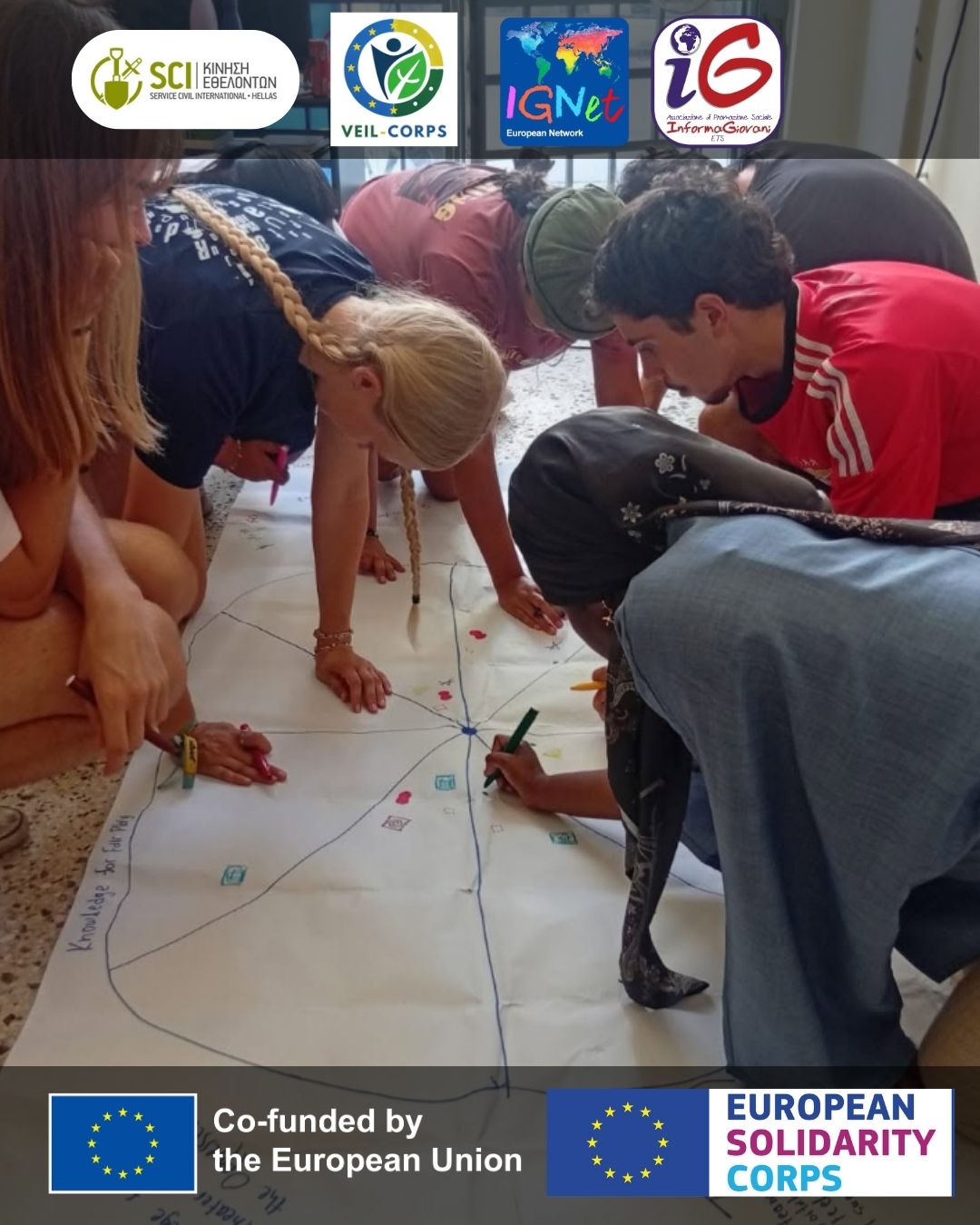 gruppo di persone che disegnano su un foglio A2, sopra e sotto l'immagine sono presenti i loghi dei partner e degli enti accreditati